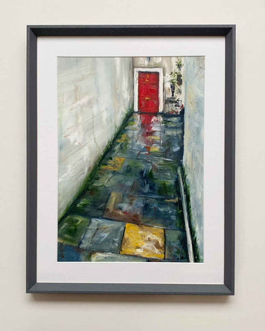 Framed painting of paved alleyway with red door in the rain
