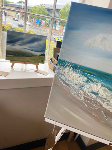 Close up of seascape painting with a smaller landscape painting on the windowsill behind it