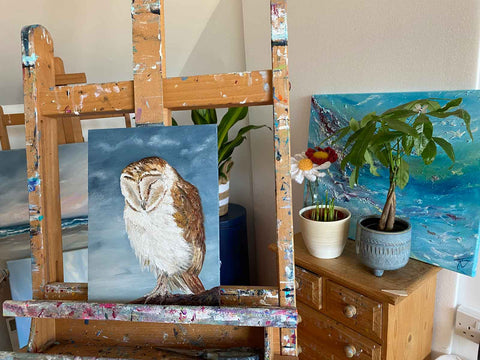 Barn owl painting on easel in front of drawers with pot plants and other paintings