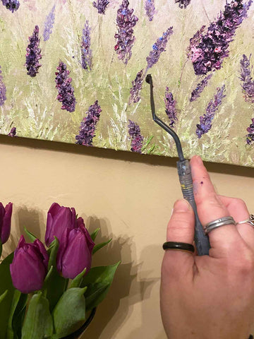 Hand holding palette knife in front of painting hanging above vase of tulips
