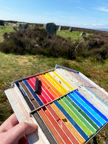 Box of pastels held up in front of standing stones
