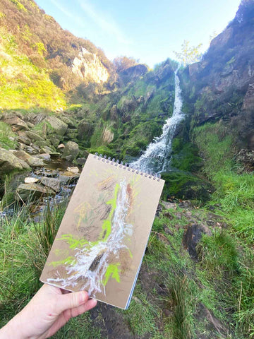 Sketch of waterfall held up in front of waterfall in gorge