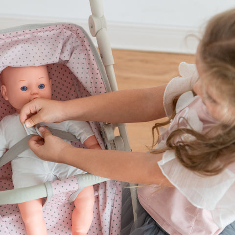 A little girl fastens the seatbelt of her doll's stroller, keeping her safe.