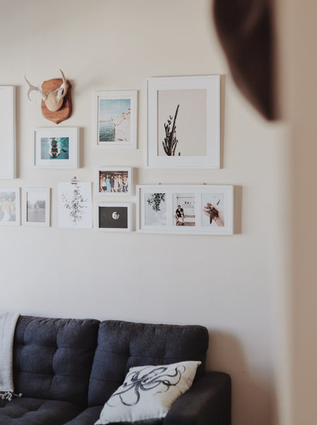 A white wall with framed art prints and a 3D sculpture right above a navy blue couch