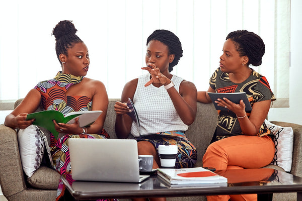 Three African creatives seated on a couch and talking to each other.