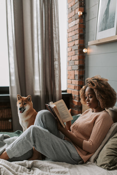 Female artist relaxing at home while reading a book with her dog.