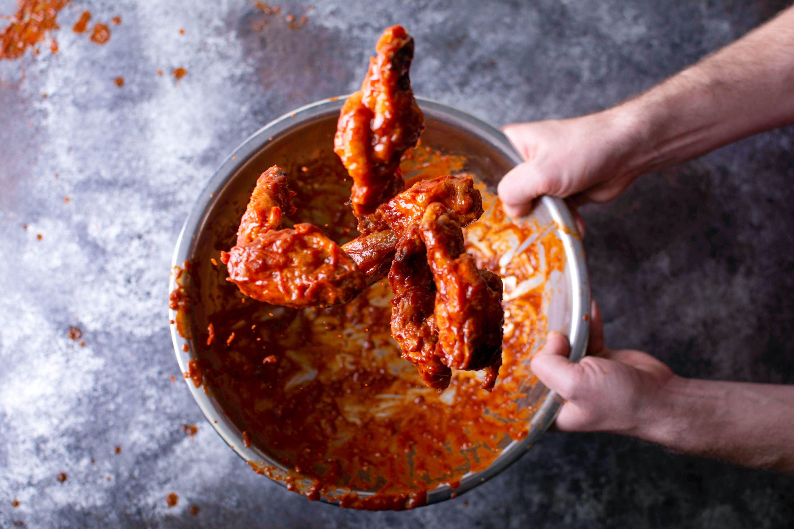 Chicken hot wings being tossed in bowl of hot sauce