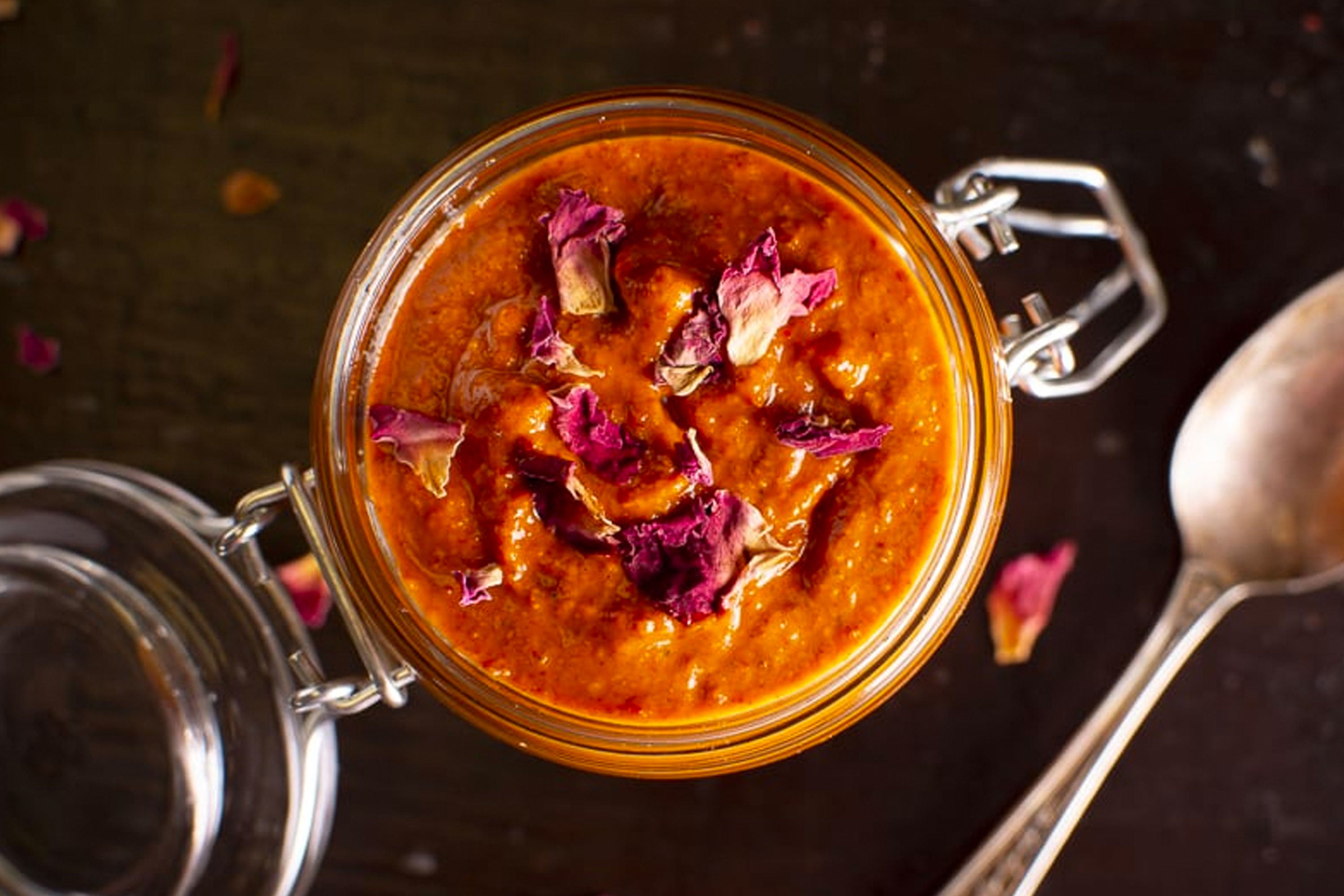 Rose harissa in an open jar with a black background and spoon to the right