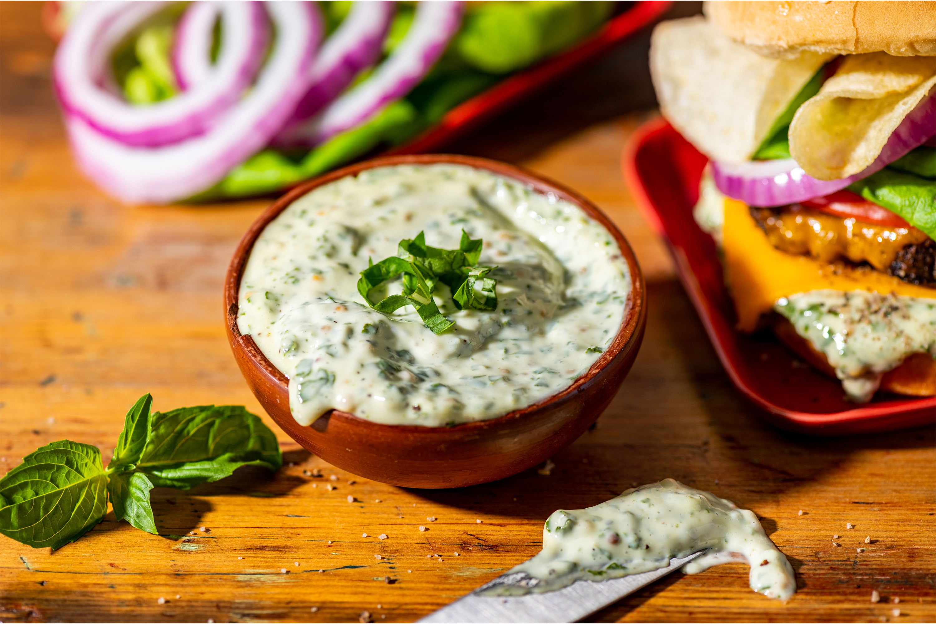 Basil Mayo in a bowl on a wooden cutting board surrounded by burger toppings