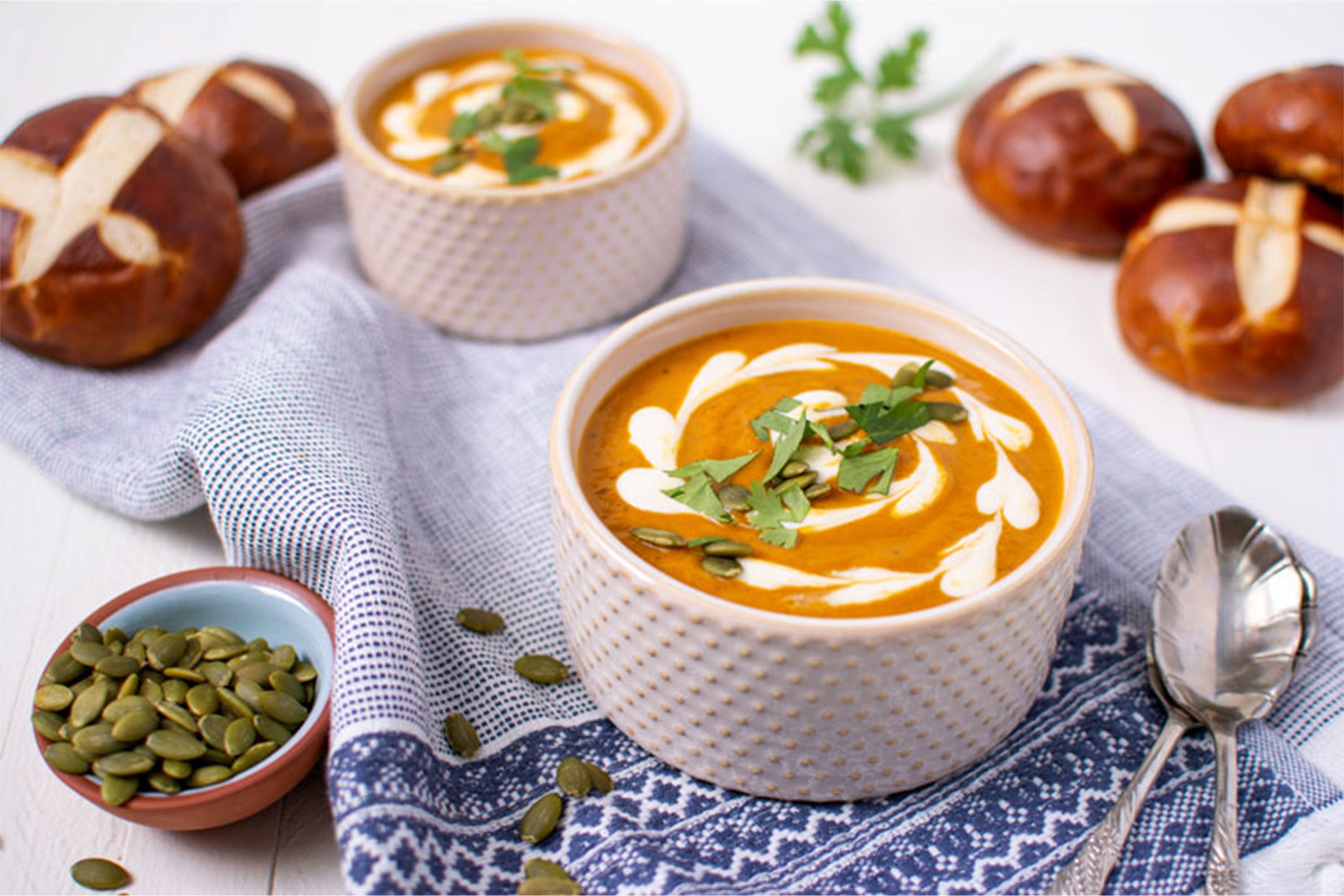 Two bowls of Chipotle Pumpkin Soup with pretzel buns in background