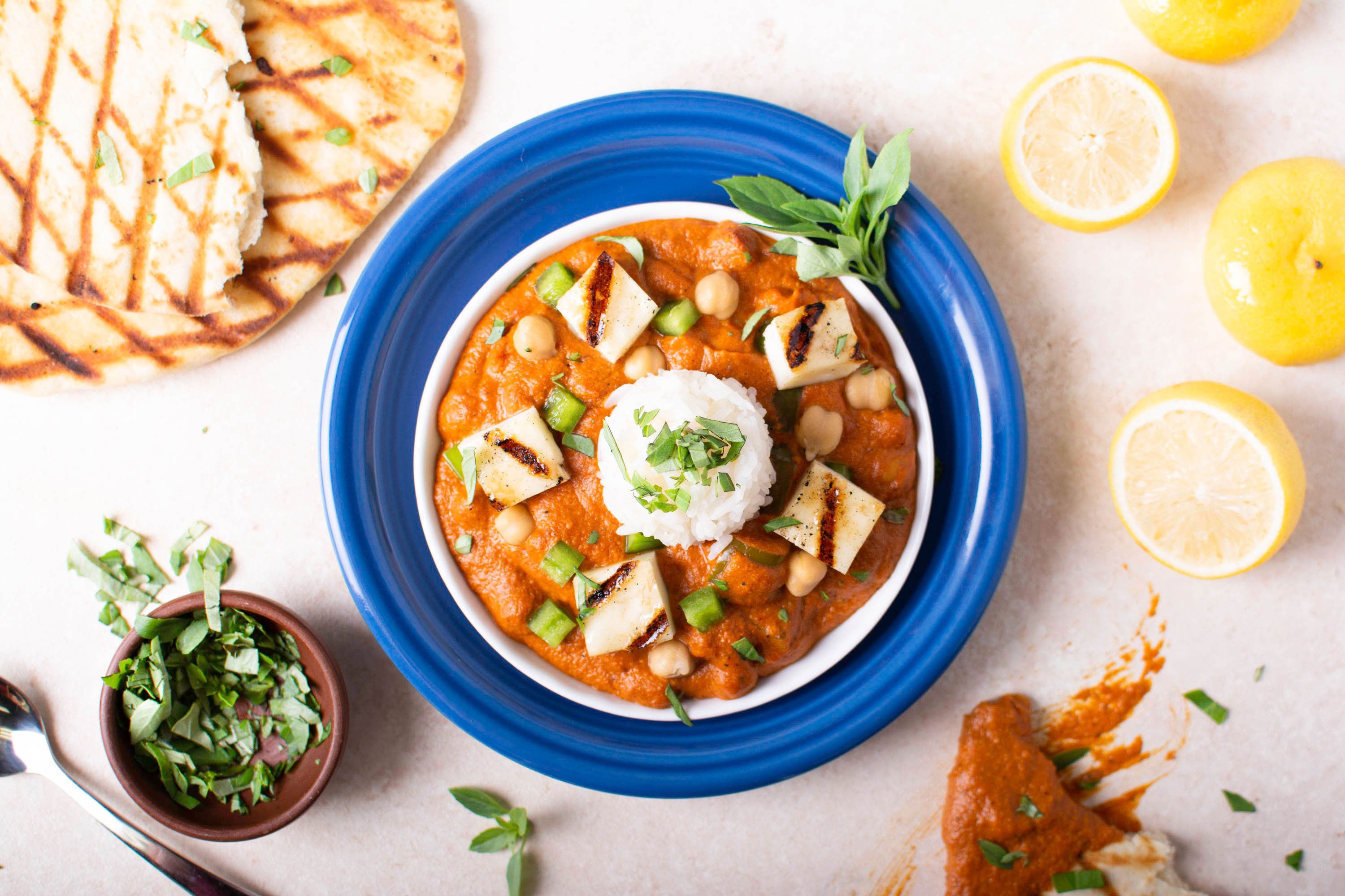 Halloumi Tikka Masala with grilled naan, lemon slices, herbs, and curry paste