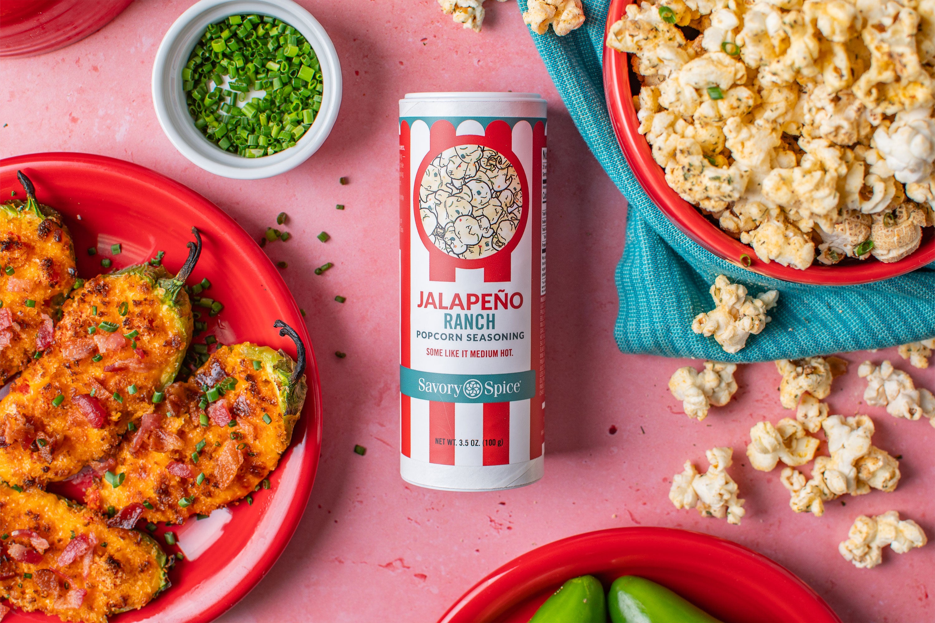 Jalapeno Ranch Popcorn Seasoning on a pink background with jalapeno poppers at the lower left and popcorn at the upper right