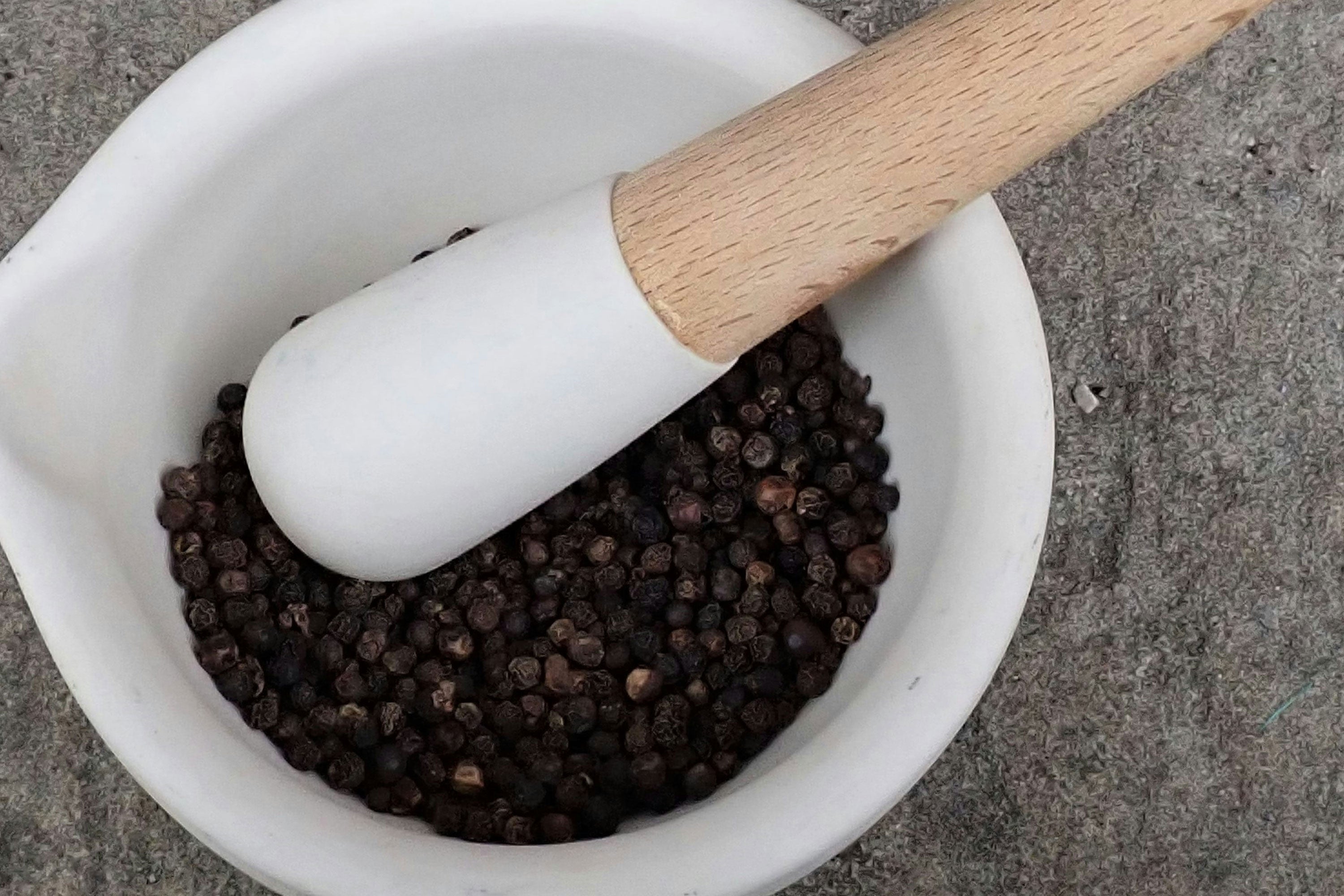 White mortar and pestle with black peppercorns