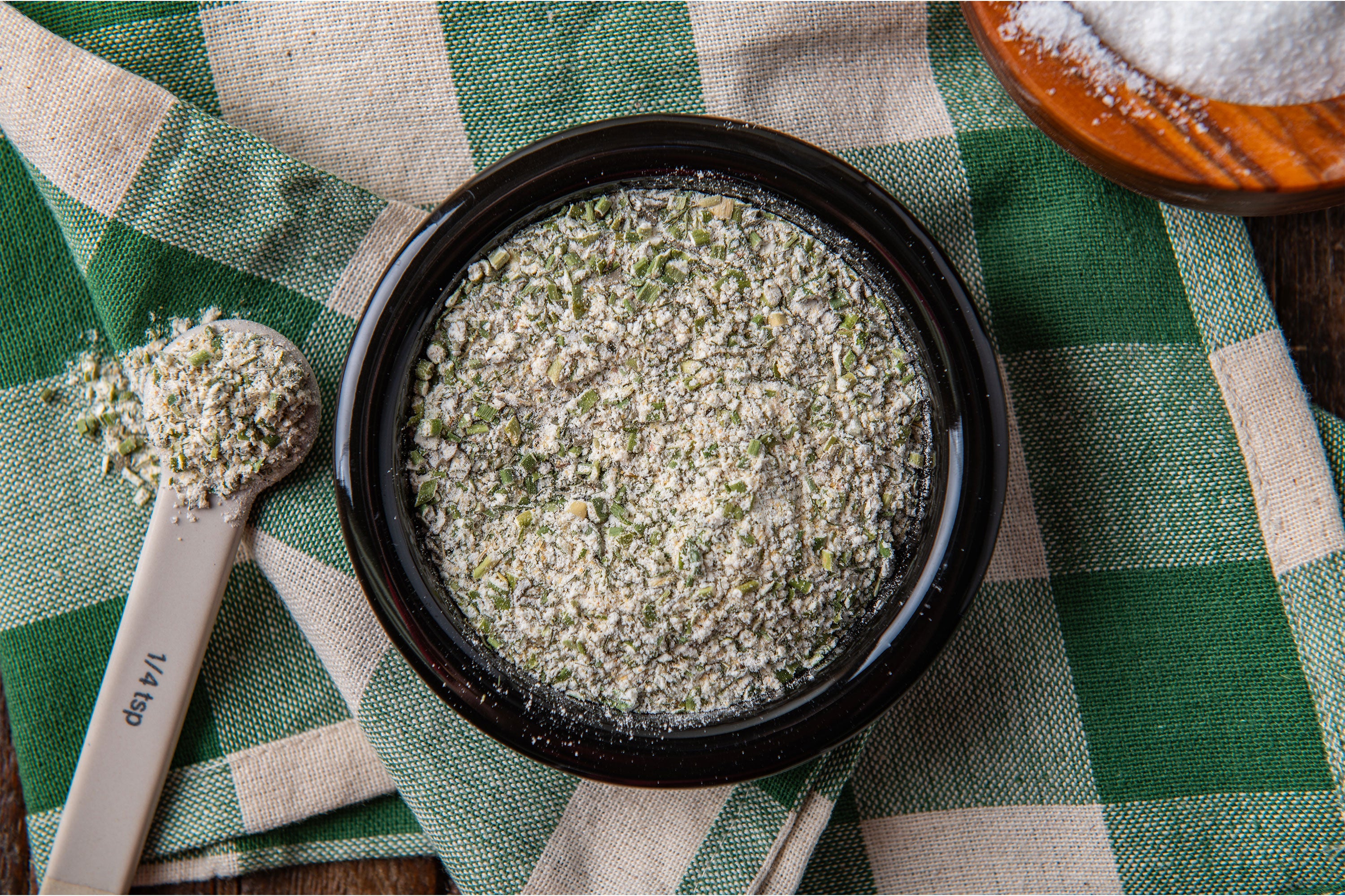 Paris Cheese Sprinkle in a bowl on a green and white plaid tablecloth with measuring spoons