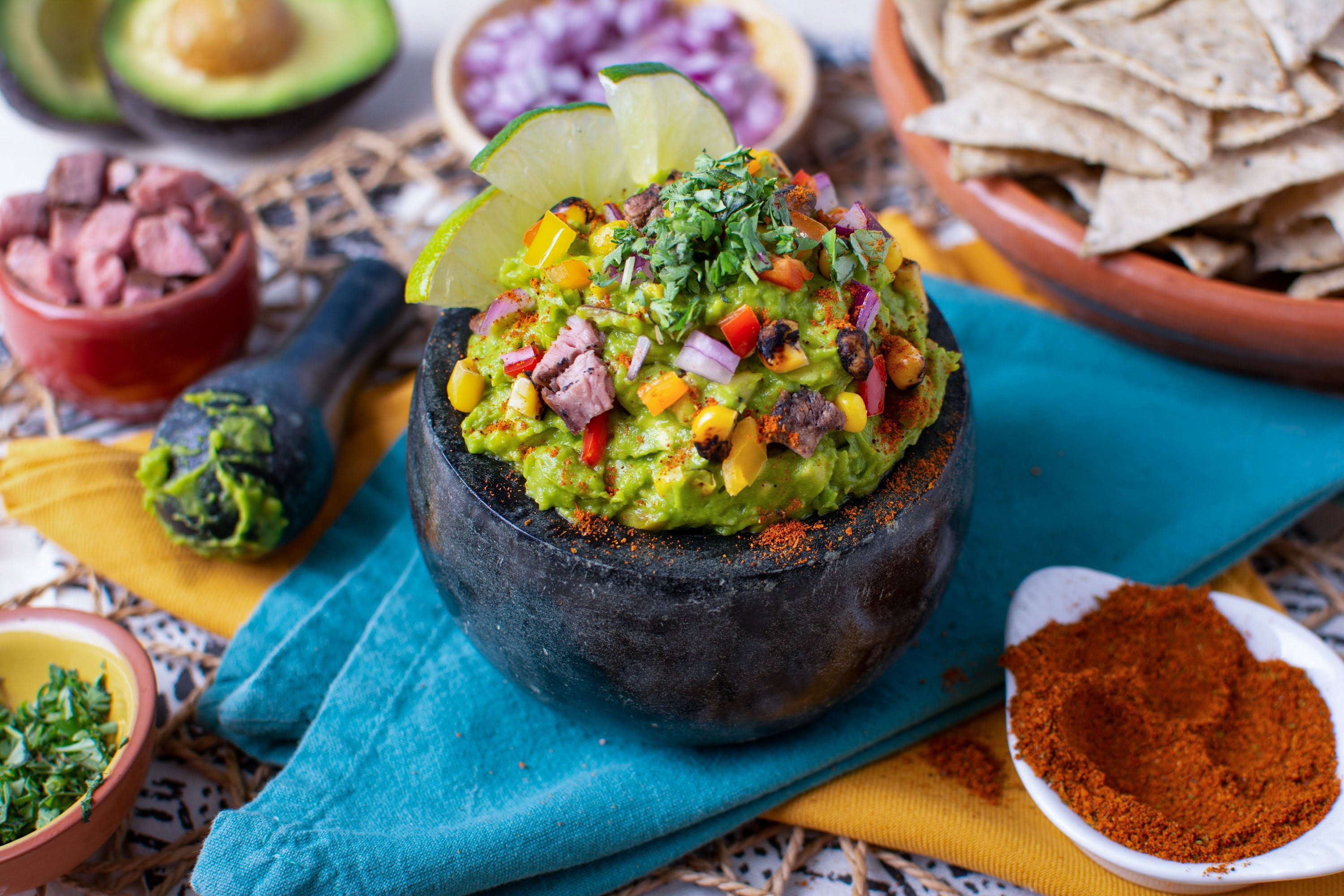 Guacamole in molcajete with assorted toppings in bowls around it