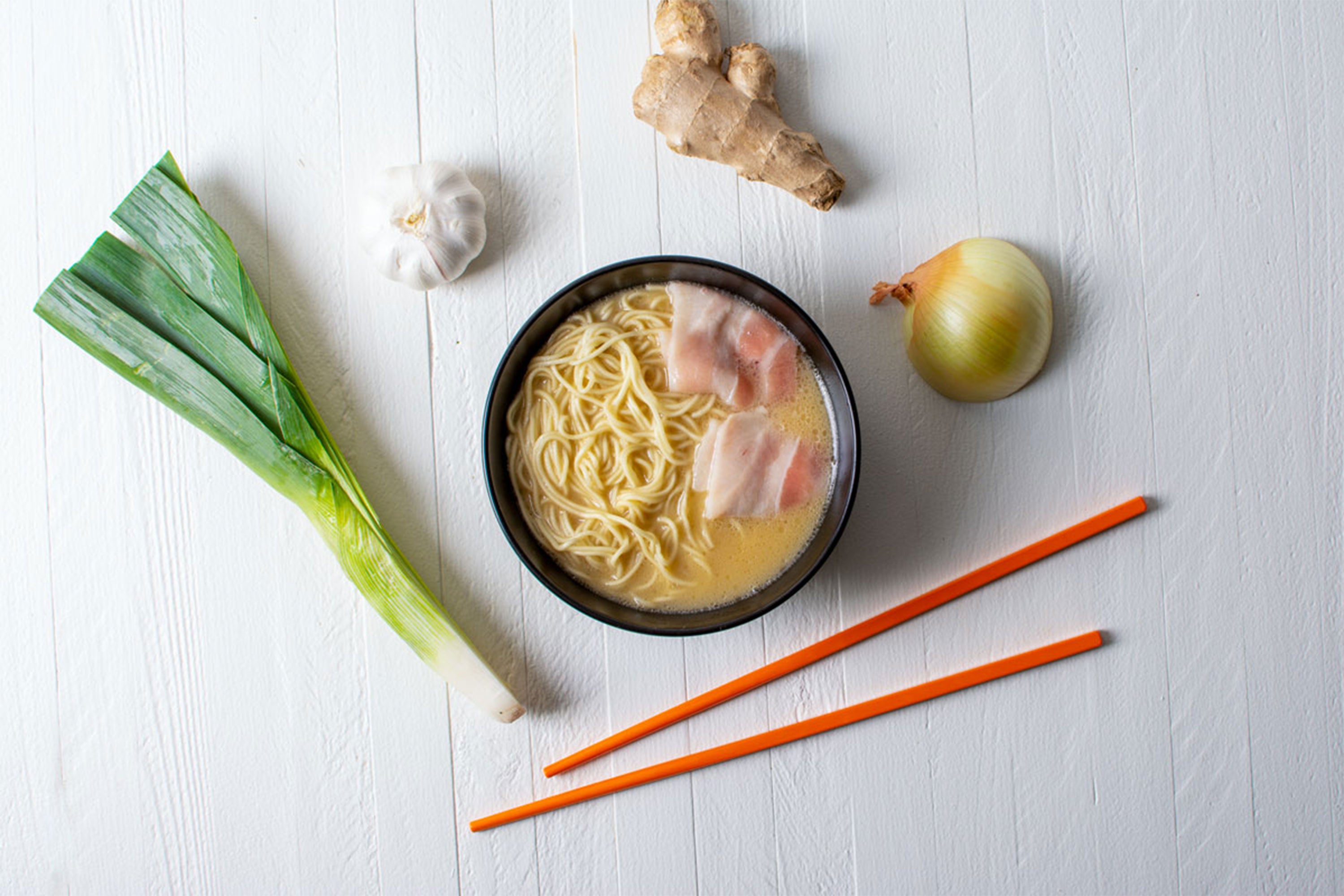 Bowl of ramen with (clockwise from left) green onion, garlic, ginger, onion, and chopsticks