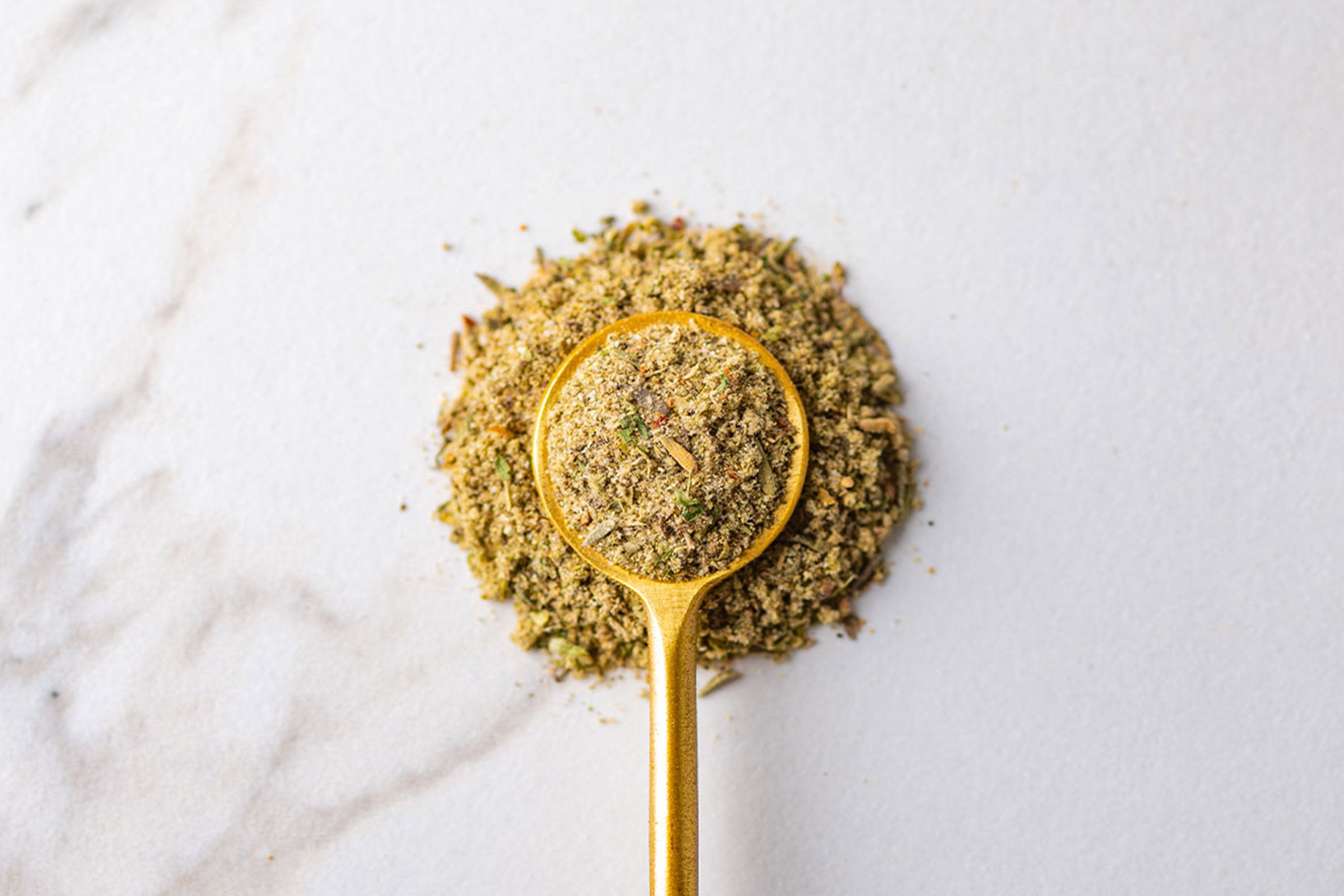 Close up of Poultry Seasoning in gold spoon on marble background