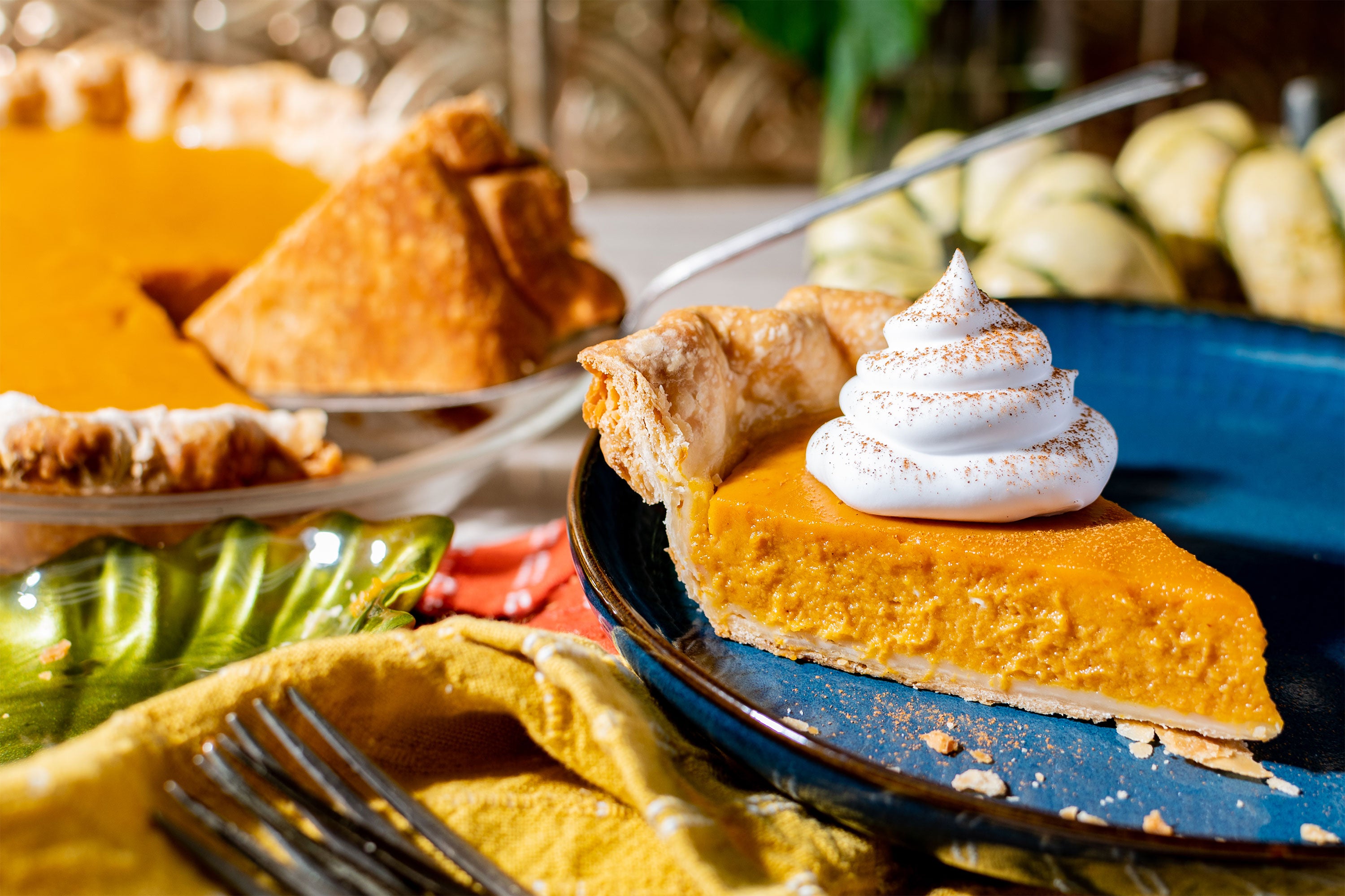 A slice of pumpkin pie with whipped cream dollop and whole pie in background