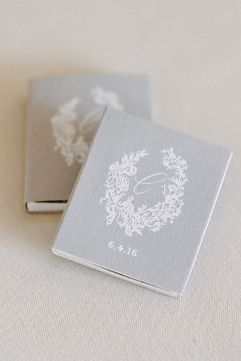 gray matchbox with white monogram crest and wedding date