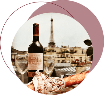 Two glasses of wine, fresh French bread, and a bouquet of flowers on a table, with the Eiffel Tower in the background.