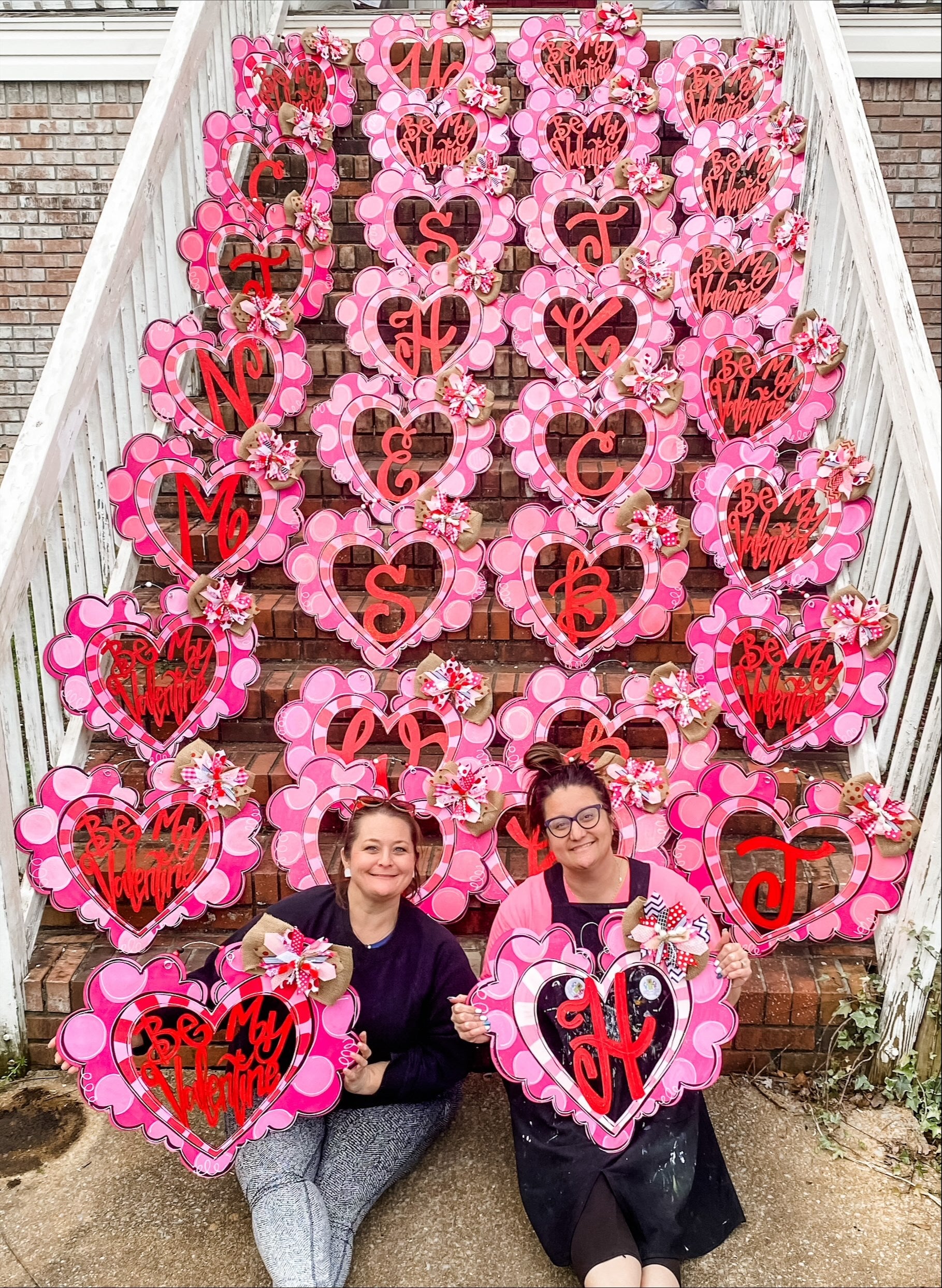 The creators of Queen of My Castle Designs with many heart-shaped door hangers propped against steps