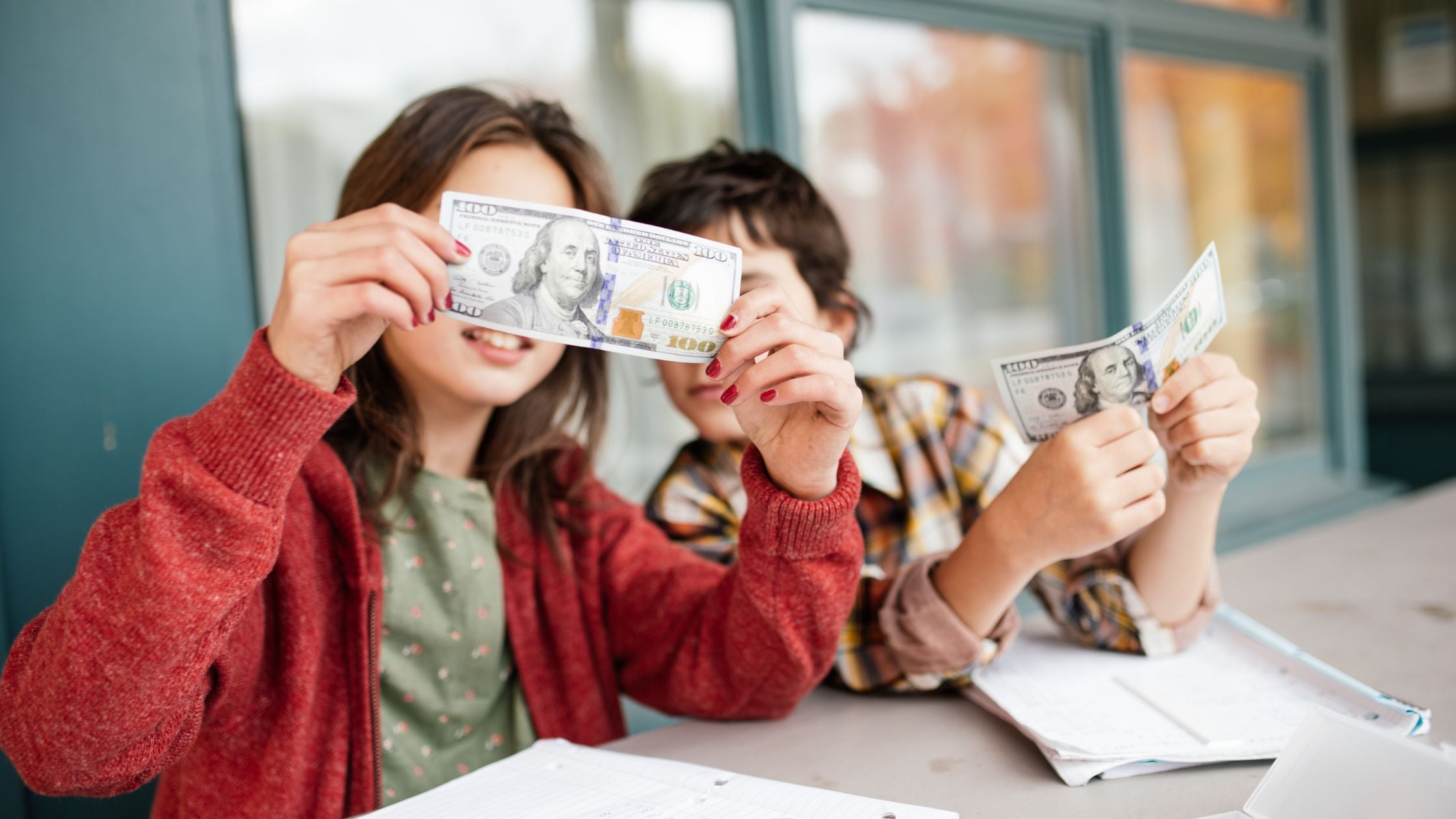 2 students sitting at a desk with notebooks and looking up close at money bills,