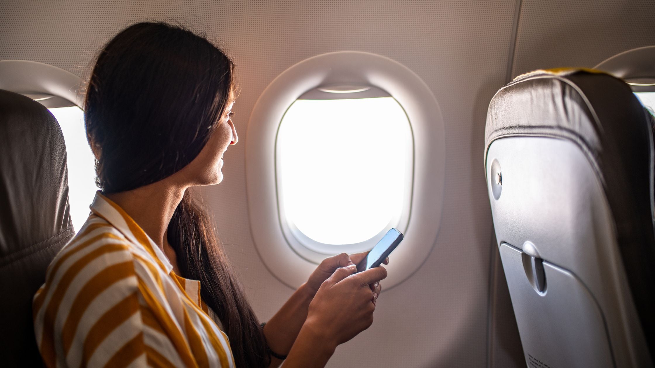 autistic adult on their phone while sitting in the window seat on a plane.