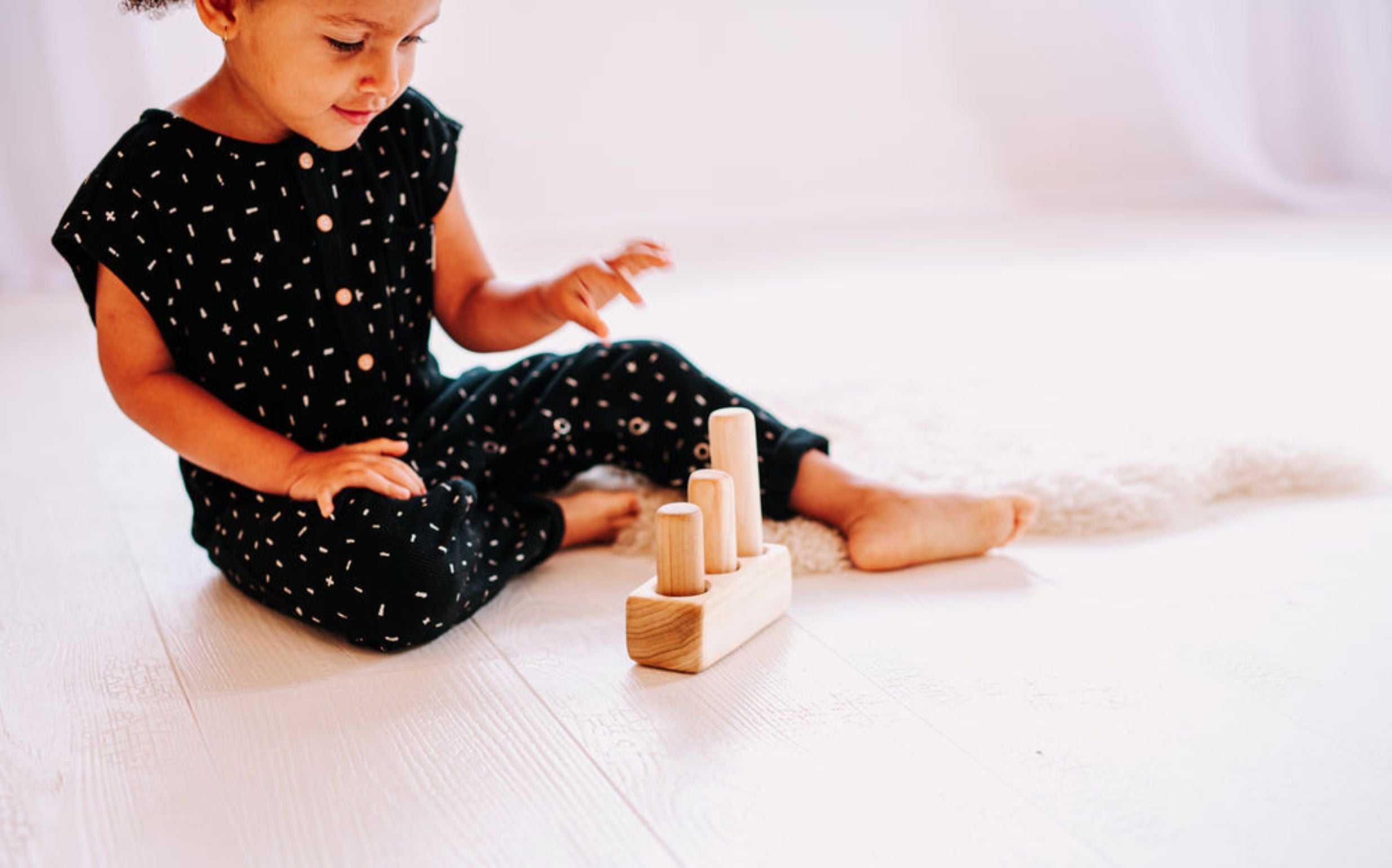 Toddler girl sits on the floor playing with the wooden Peg Puzzle Toy by Clover & Birch.