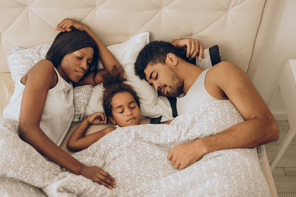 child is sleeping with her parents