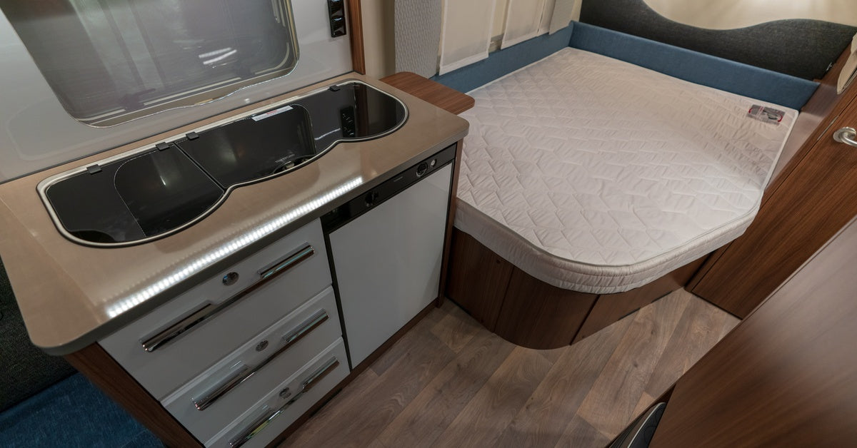 An aerial view of the inside of a small mobile home. The kitchen area sits immediately next to the bed.