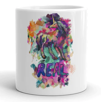 A coffee mug from Real Unicorn Apparel with a stylized unicorn as the main design and the word "Real" written underneath.