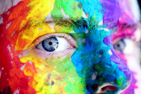 A person with striking blue eyes and a rainbow-painted face. 