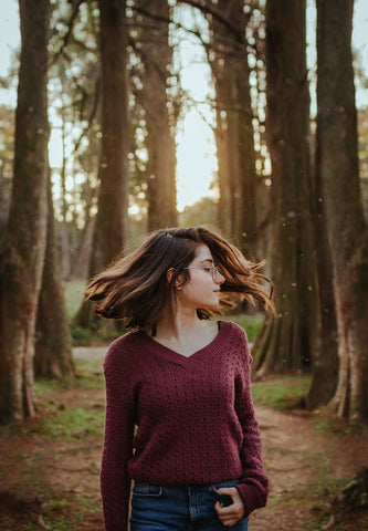 A woman with glasses waving her hair while walking through a forest.