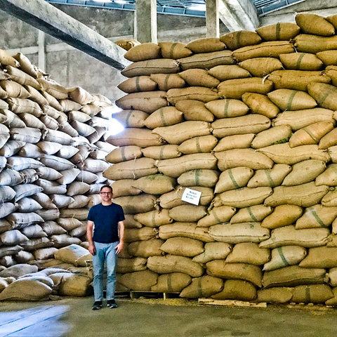 Mark Smutek standing next to large stack of green coffee bags