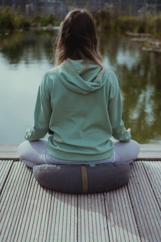 Girl meditation on a crescent zafu pillow on a lake side in a lotus pose sitted meditation