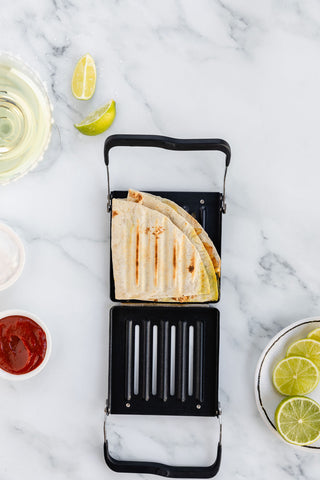 Revolution Panini Press open on the counter with a toasted Triangle fold quesadilla inside. limes and salsa next to it