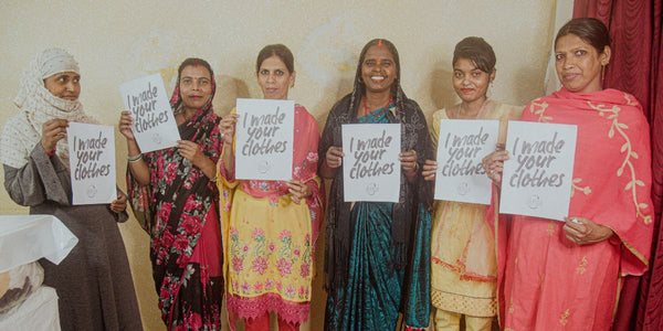 A group of female artisans from India holding a banner that reads "I made your clothes".