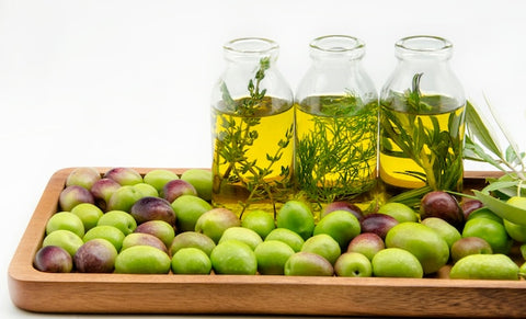 A captivating overhead shot of a rustic wooden table with a glass bottle of extra virgin olive oil elegantly positioned in the center. Surrounding the bottle are fresh olives, a sprig of rosemary, and a loaf of crusty bread, creating an inviting tableau that sets the stage for the article.