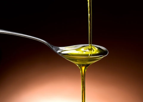 A close-up of a droplet of extra virgin olive oil falling into a spoon, capturing the rich, golden color of the oil. Graphical overlays or text could highlight key antioxidants like polyphenols and vitamin E, underlining the nutritional benefits discussed in the section.