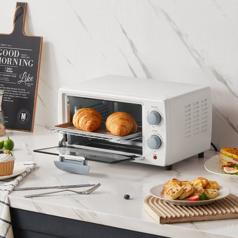 An open black mini oven with two croissants inside, surrounded by pizza and cake