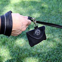Hand holding Tre Ponti Mesh Leash with Mesh Bag Dispenser in black with background of manicured grass