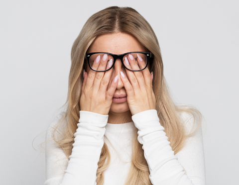 blonde woman rubbing eyes behind glasses