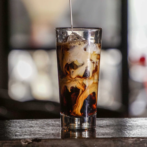 Milk poured on a White Russian cocktail on a Collins glass