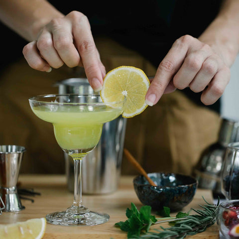 Woman putting lemon wheel garnish on cocktail on a coupe glass