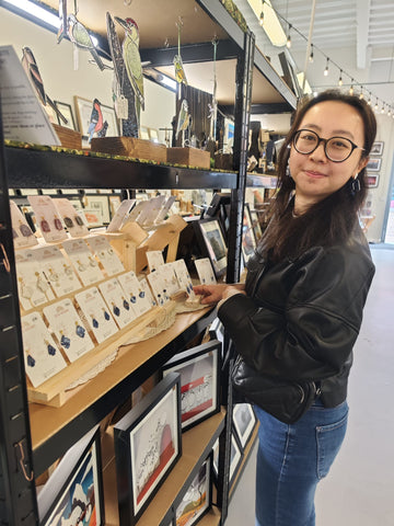 Asian maker stood by a clay earrings display in a gift shop