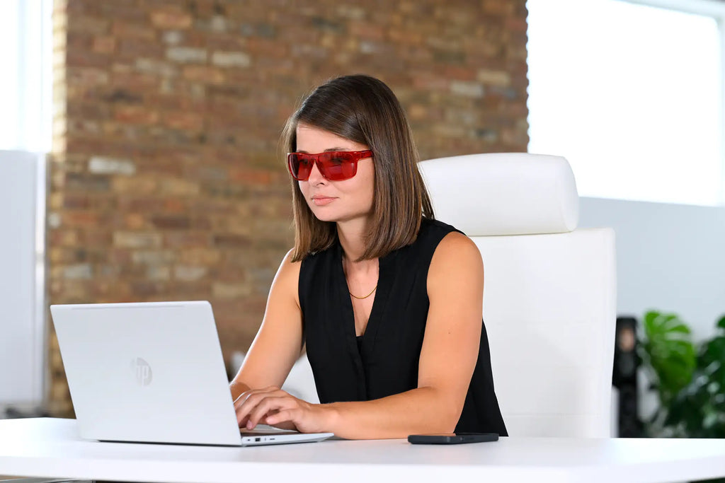 Neuroathletiktrainerin sitzt mit einer roten ARTZT neuro Farbbrille vor einem Laptop.