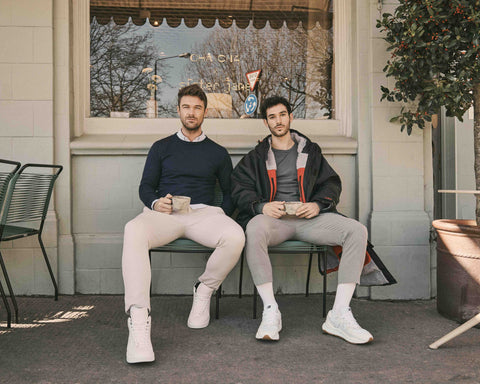 Two men sitting in a cafe in London drinking coffee wearing extra-fine merino wool knit jumpers with a fleece-lined, waterproof, weatherproof outdoor robe that is functional and stylish. 