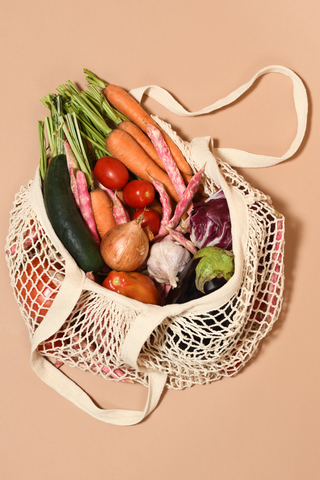 A white mesh produce bag containing fresh veggies against orange background