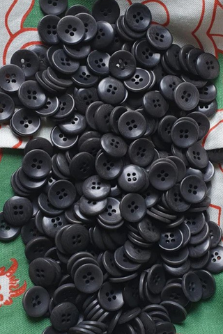 Hundreds of plastic-free Coroza buttons are laid on top of Wild Clouds green clouds fabric