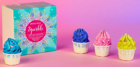 Four bath melts of various colors set on a pink table and pink backrdrop. There is a turquoise giftbox that says Sparkle.